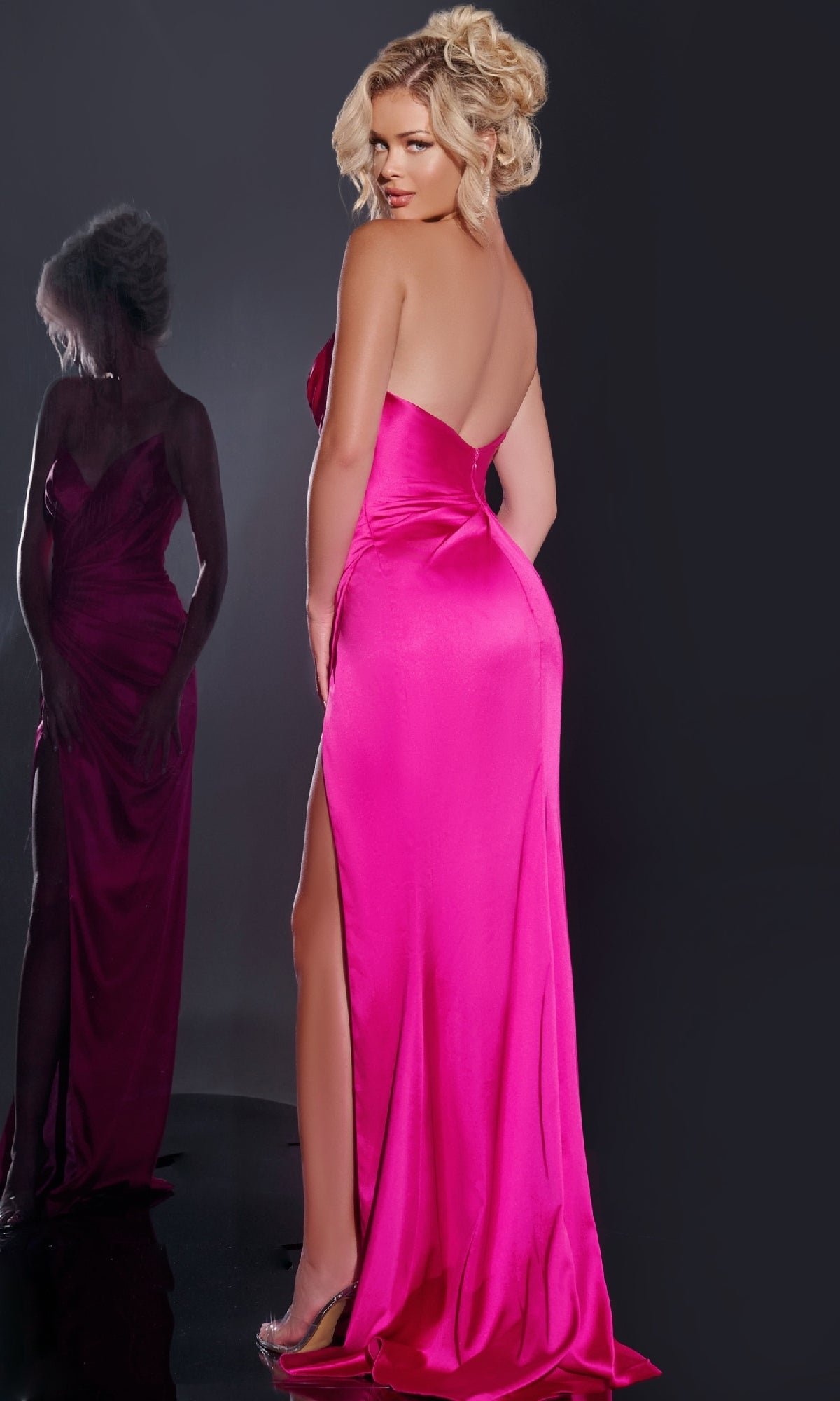 A woman in the Jovani 37079 long prom dress, a bright pink strapless gown with a high slit, stands with her back to the camera, looking over her shoulder as her reflection appears in the mirror.